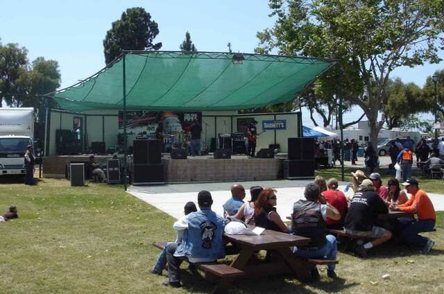 A band performing on an outdoor stage at a motorcycle rally in Santa Maria, California, with bikers gathered at picnic tables