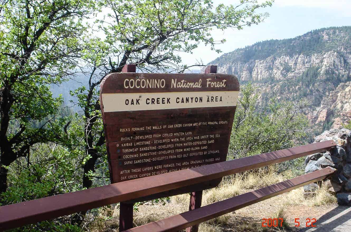 The Coconino National Forest, Oak Creek Canyon Area sign, with red and white canyon cliffs behind