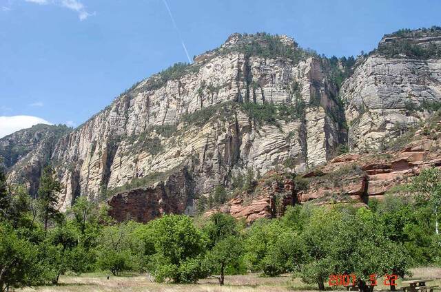 Striped sandstone cliffs rising above a green canyon floor in Oak Creek Canyon, Coconino National Forest