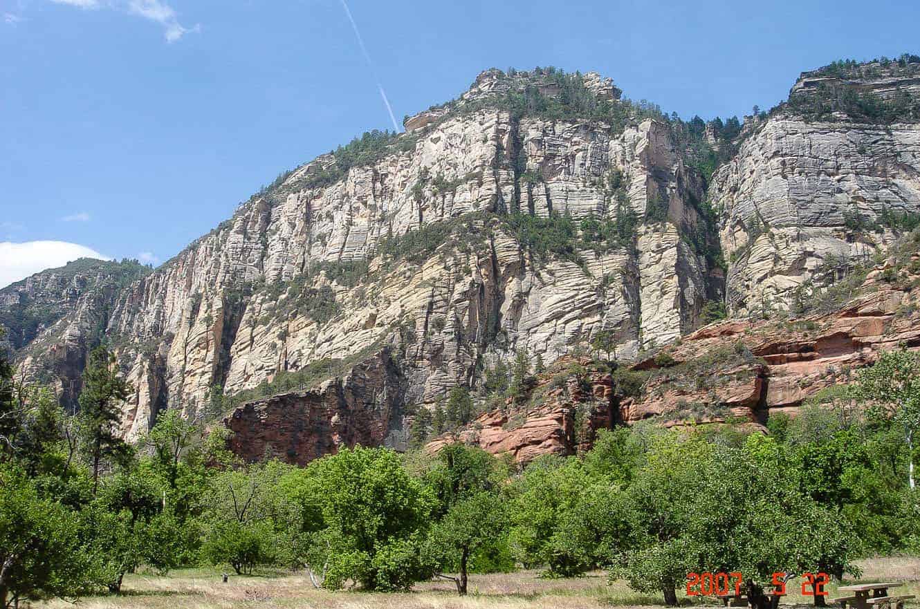 Striped sandstone cliffs rising above a green canyon floor in Oak Creek Canyon, Coconino National Forest
