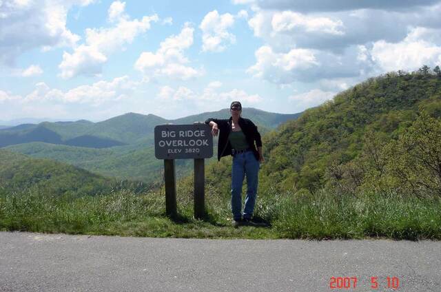 Standing beside the Big Ridge Overlook sign on the Blue Ridge Parkway, elevation 3,820 feet, with rolling green mountains behind
