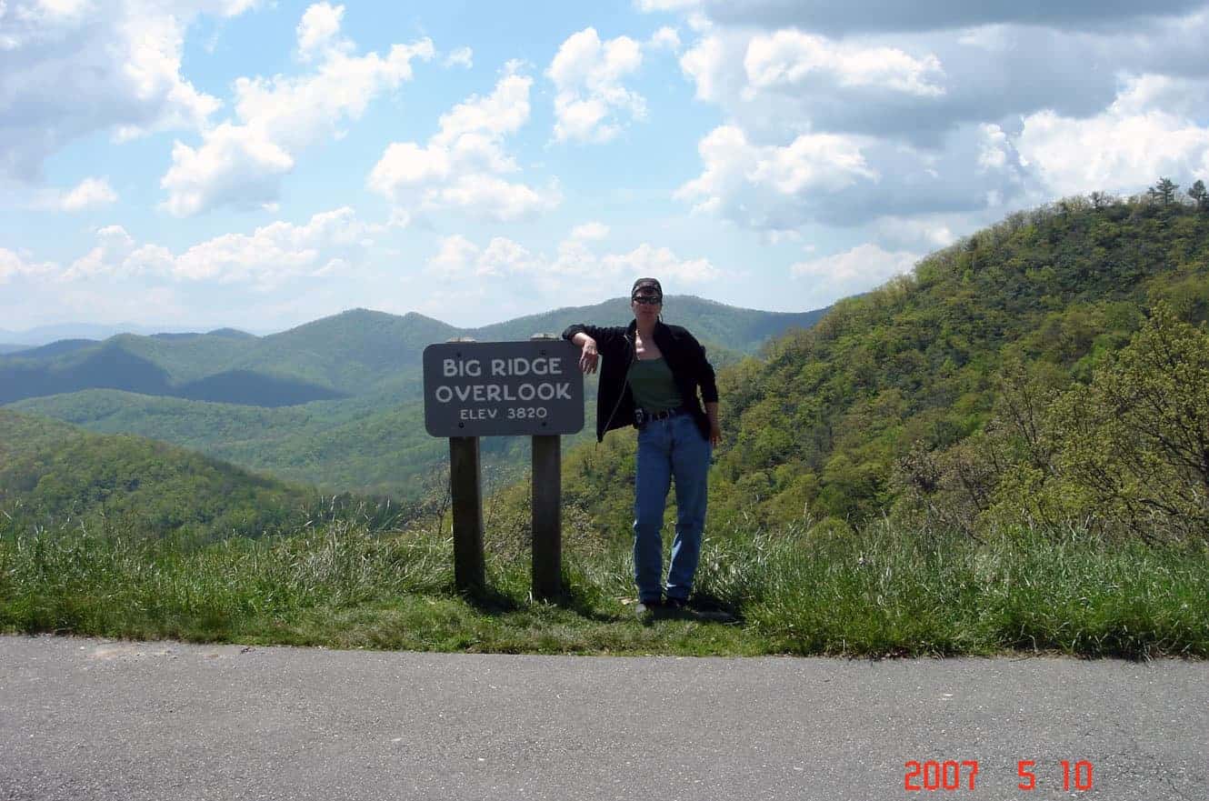 Standing beside the Big Ridge Overlook sign on the Blue Ridge Parkway, elevation 3,820 feet, with rolling green mountains behind