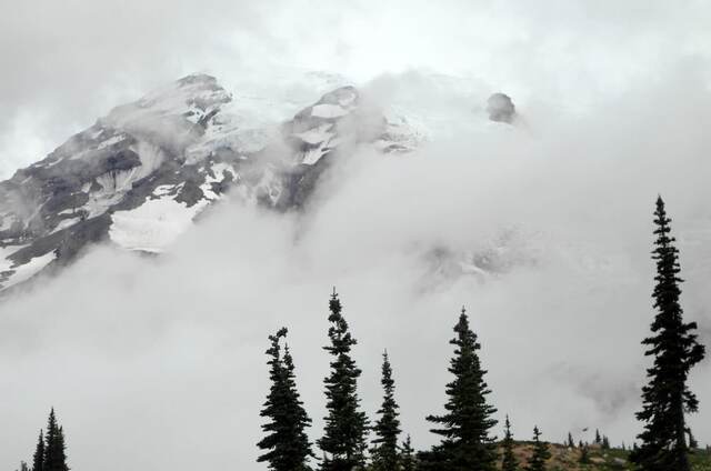 Mount Rainier's snow-covered slopes and glaciers emerging through swirling clouds