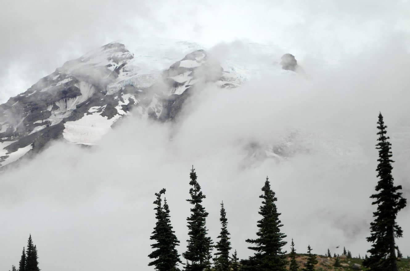 Mount Rainier's snow-covered slopes and glaciers emerging through swirling clouds