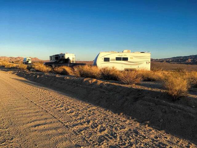 An RV trailer and truck parked in the desert scrub off a dirt road near Joshua Tree National Park at sunset