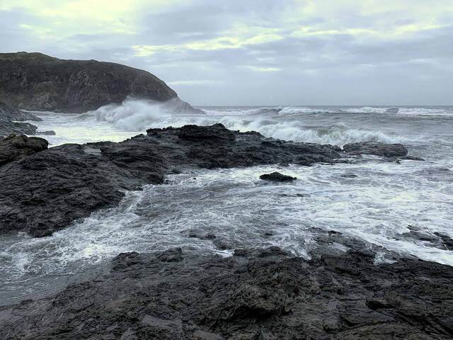 Waves crashing over dark rocks at Agate Beach under a cloudy sky