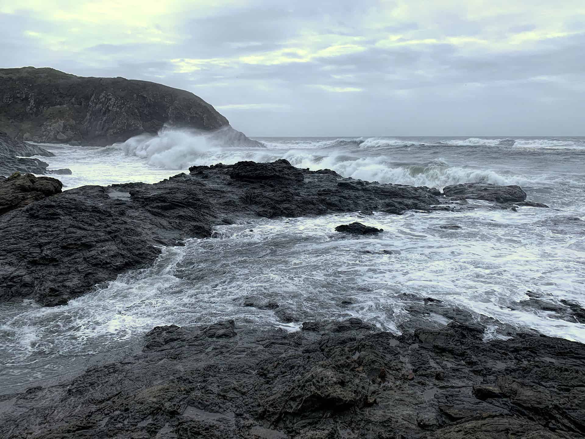Waves crashing over dark rocks at Agate Beach under a cloudy sky