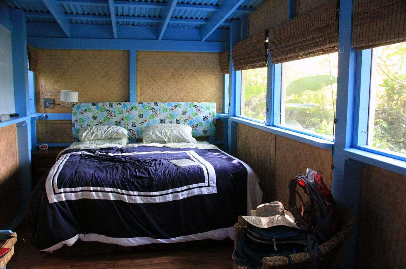 Interior of the blue-trimmed jungle cabin bedroom, with a floral headboard and packed backpacks in the corner
