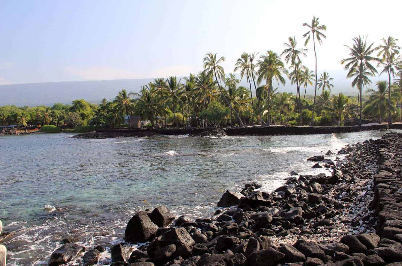Palm-lined shoreline and turquoise bay at Pu'uhonua O Hōnaunau, seen from the rocky point