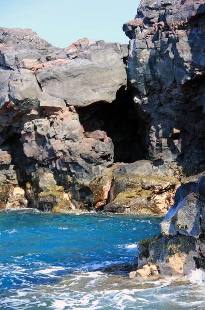 A tall, narrow sea cave carved into the rugged lava cliffs