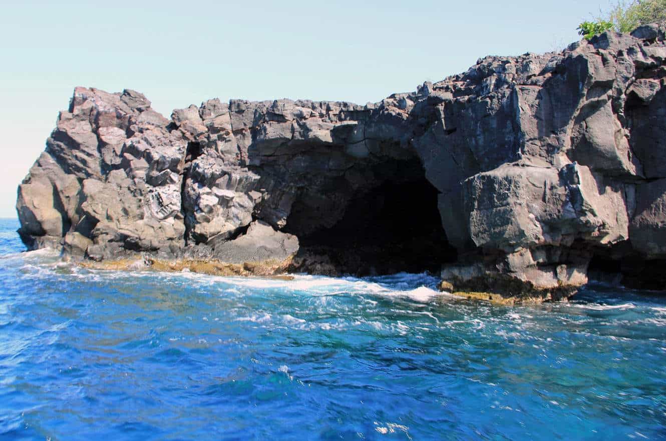 A sea cave entrance framed by grassy cliffs, with turquoise water below