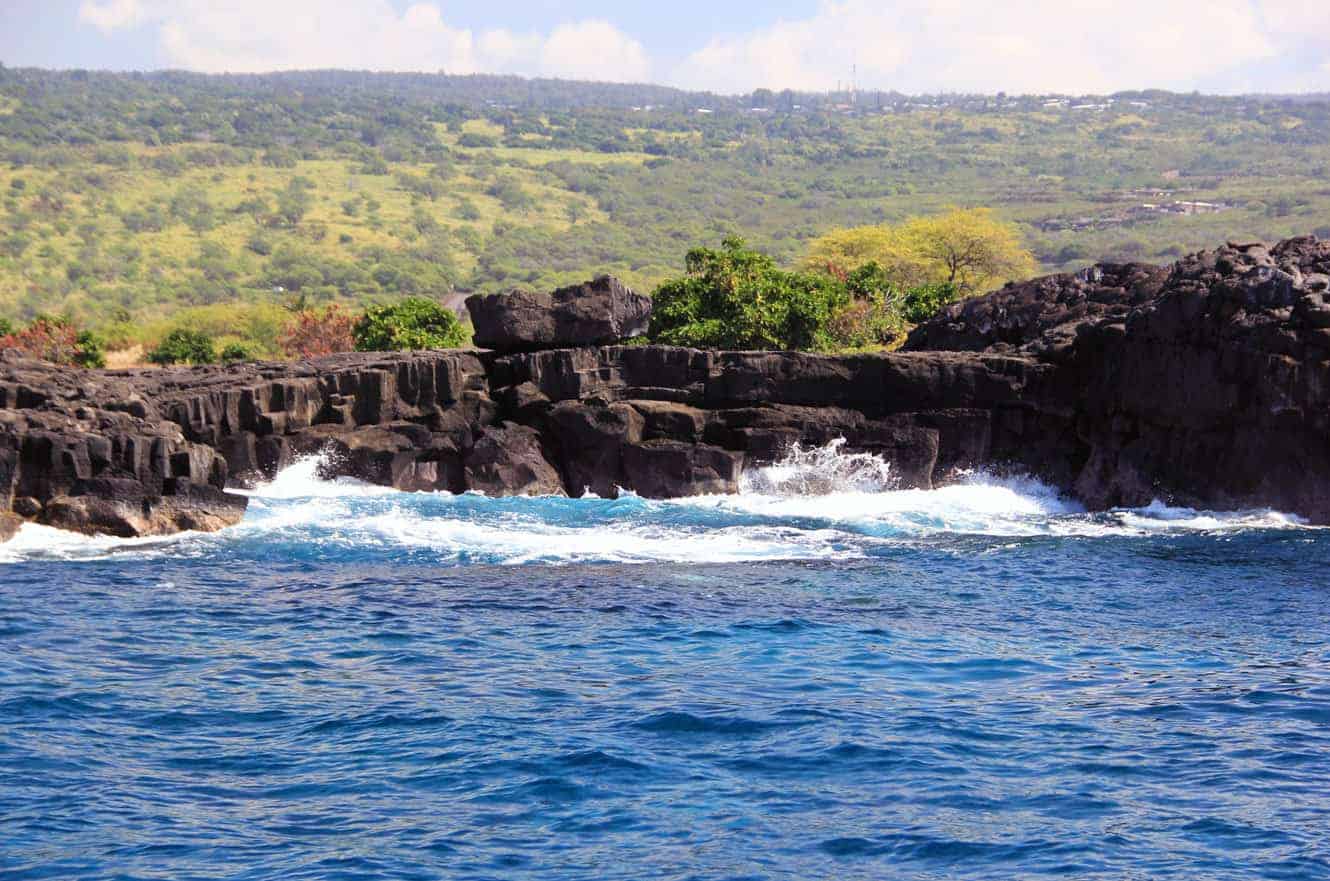 Waves breaking along the black lava coastline, with the hillside town visible in the distance