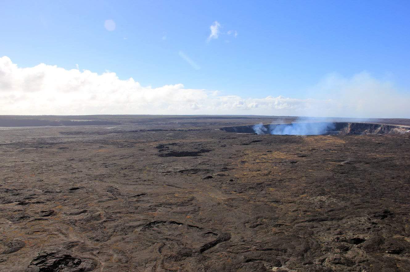 A wider view of the smoking Halemaʻumaʻu crater across the caldera floor
