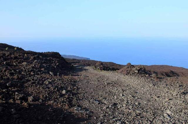 A black lava field stretching toward distant trees and the coastline