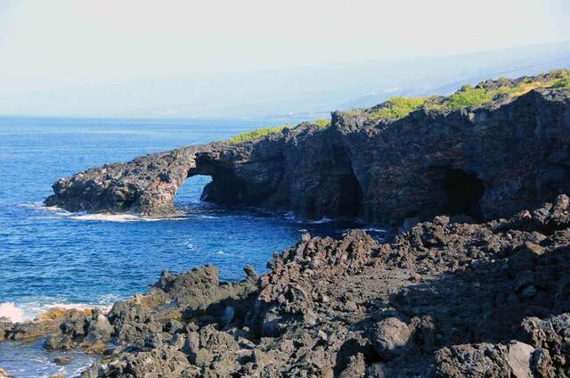 A natural lava rock arch opening onto the ocean, with dark cave openings in the cliff