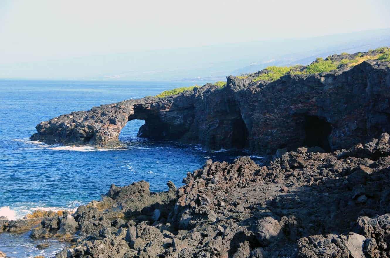 A natural lava rock arch opening onto the ocean, with dark cave openings in the cliff