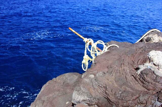 A rope tied to a metal stake wedged into the lava rock, used to climb back out of the water