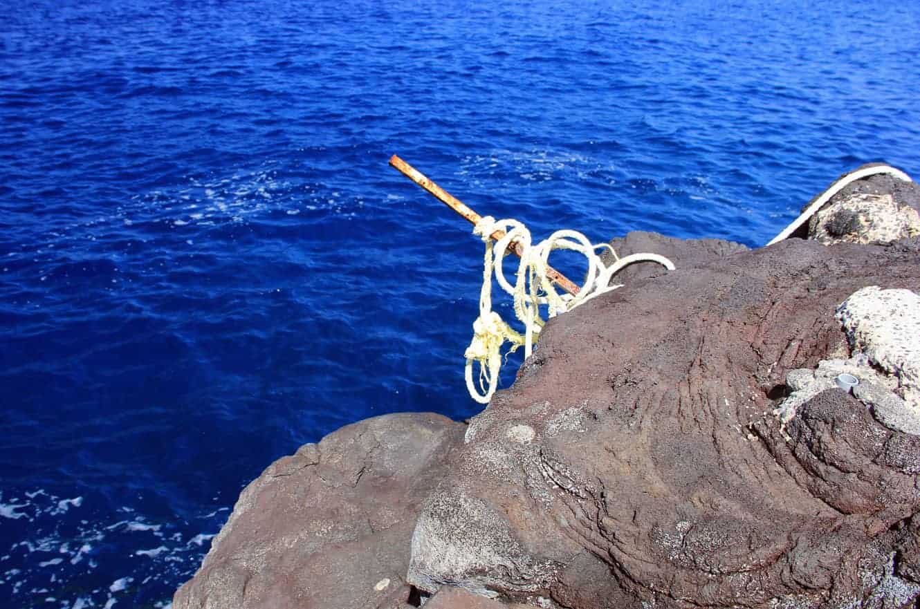 A rope tied to a metal stake wedged into the lava rock, used to climb back out of the water