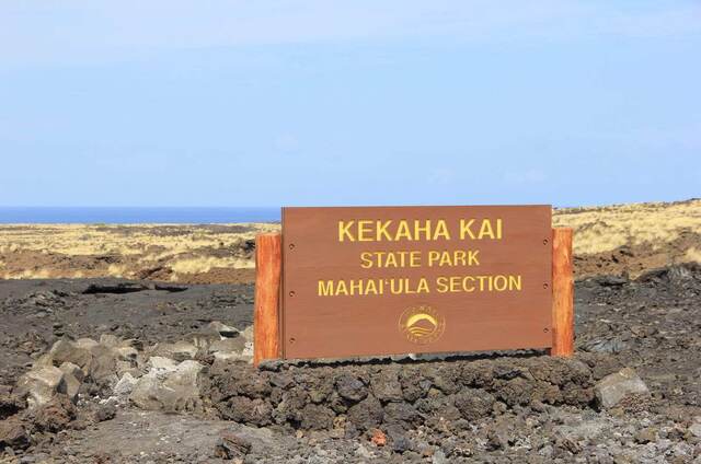 The Kekaha Kai State Park, Mahai'ula Section entrance sign amid a black lava field with the ocean beyond
