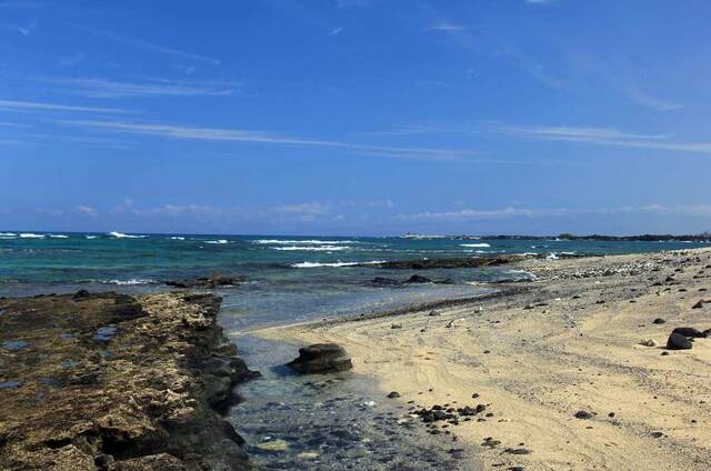 A rocky tide pool and pale sand beach along the coast at Kekaha Kai State Park