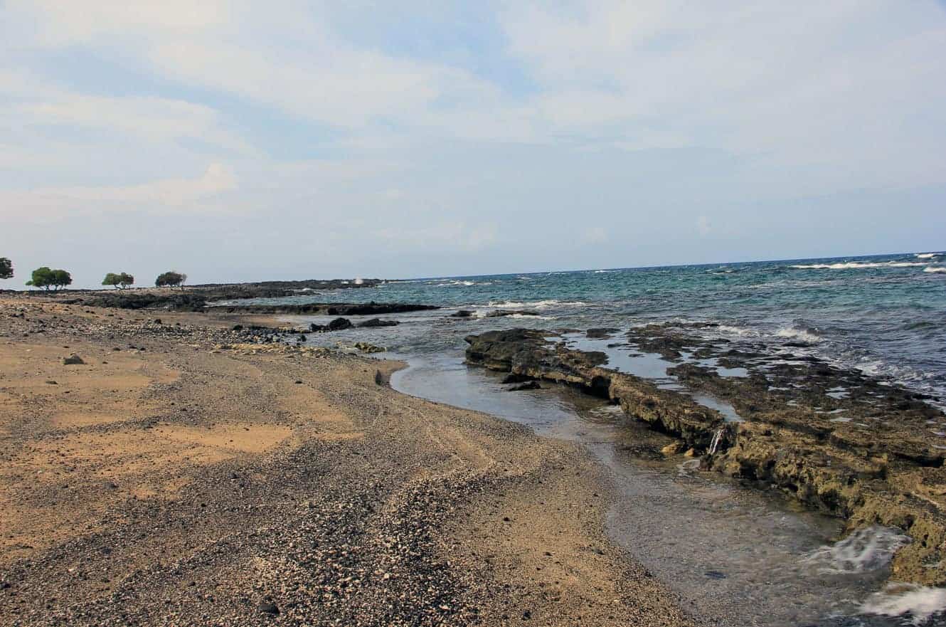 A sandy cove with scattered trees along the shoreline at Kekaha Kai State Park