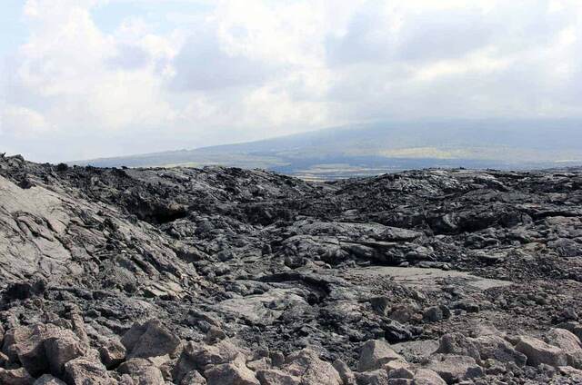 A black lava field stretching toward a hazy view of Mauna Loa in the distance