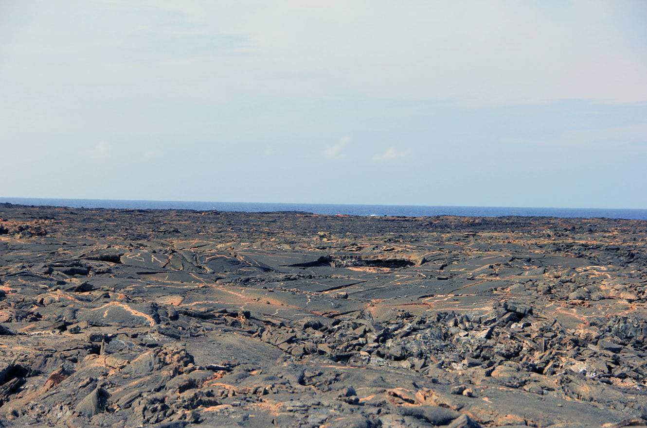 A vast black lava field with the ocean visible on the horizon
