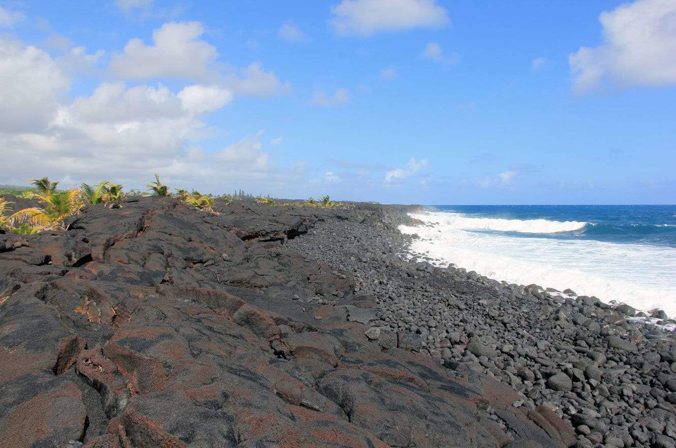 A rugged black lava rock shoreline with waves breaking along the coast