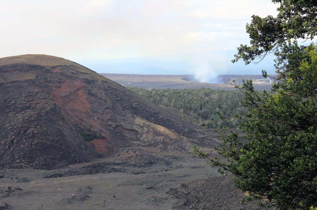 A cinder cone with steam rising from a distant crater