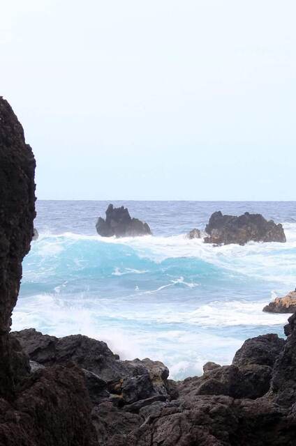 Waves crashing against dark lava rocks offshore, seen between two boulders