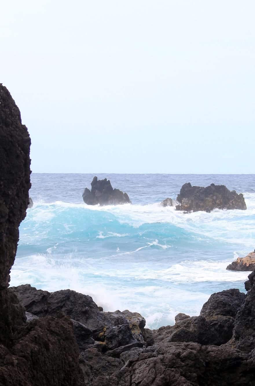 Waves crashing against dark lava rocks offshore, seen between two boulders