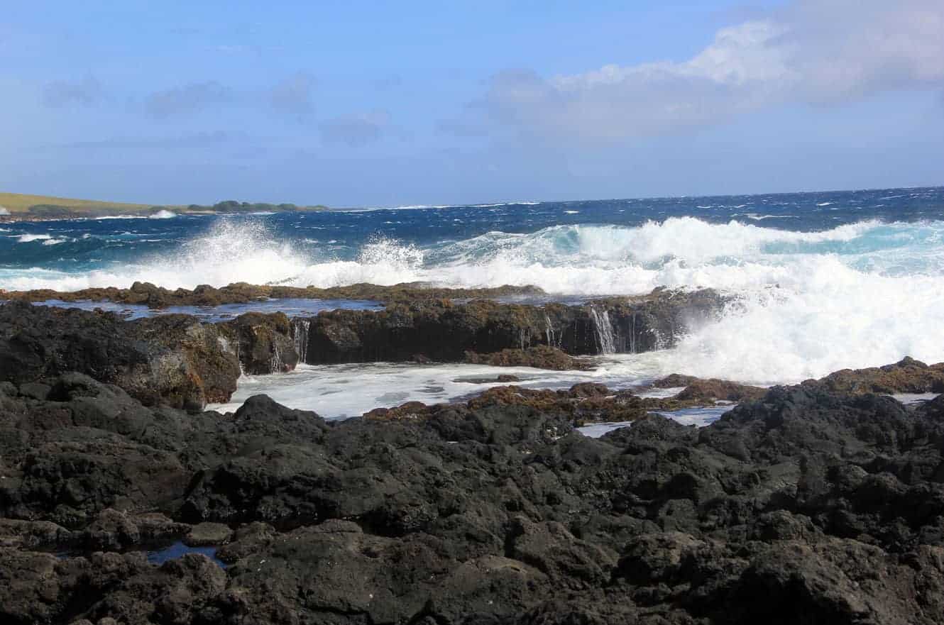 Waves crashing over a lava rock shelf along the coastline