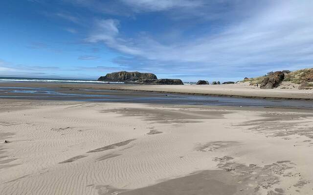 A wide sandy beach at low tide with sea stacks offshore under a partly cloudy sky