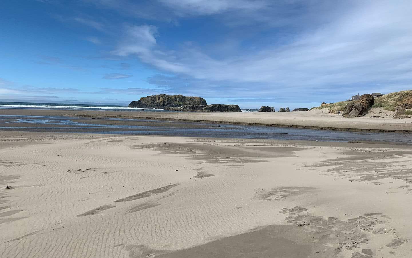 A wide sandy beach at low tide with sea stacks offshore under a partly cloudy sky